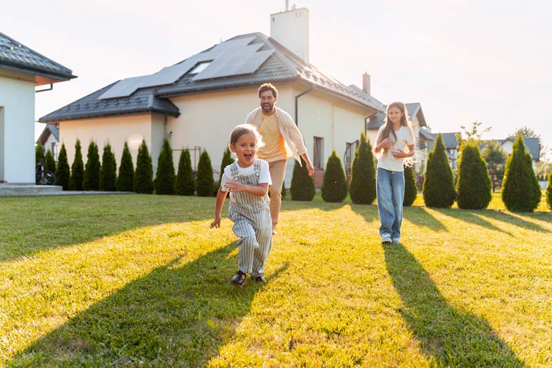Family home with solar panels Family enjoying the outdoors in front of a home with solar panels